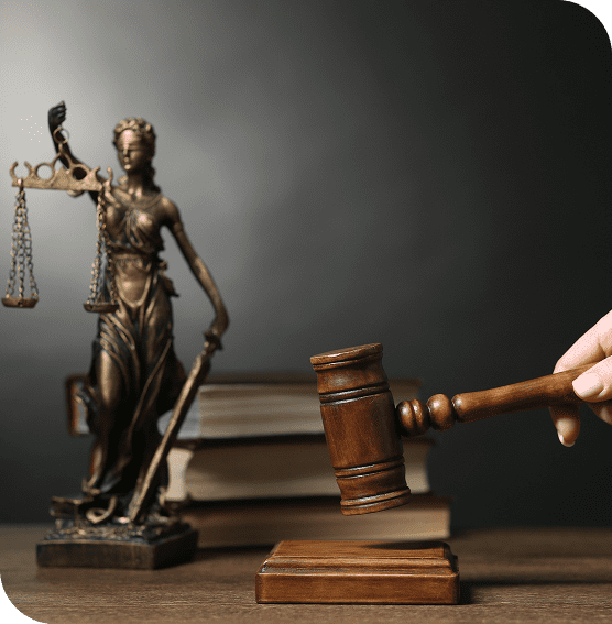 A hand holding a gavel over a wooden block, with a statue of Lady Justice and law books in the background.